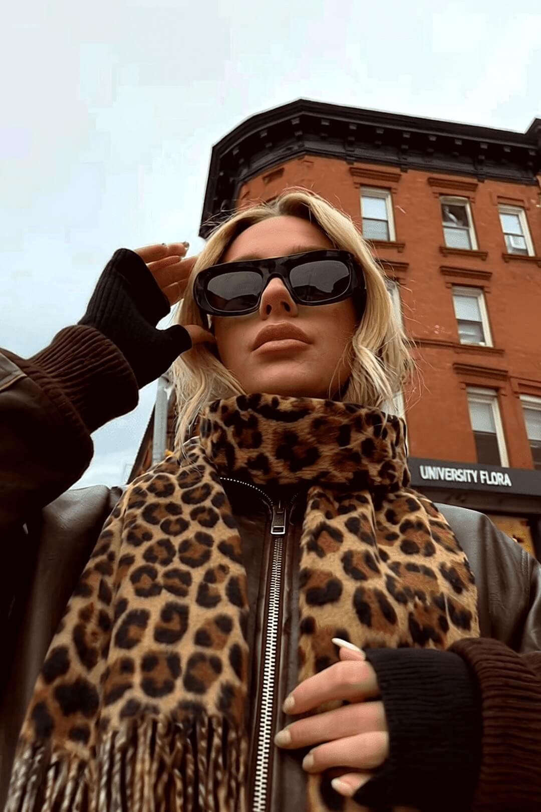 Marais leopard scarf low-angle editorial against a red-brick building, 90s-style sunglasses — Amavé winter scarf.