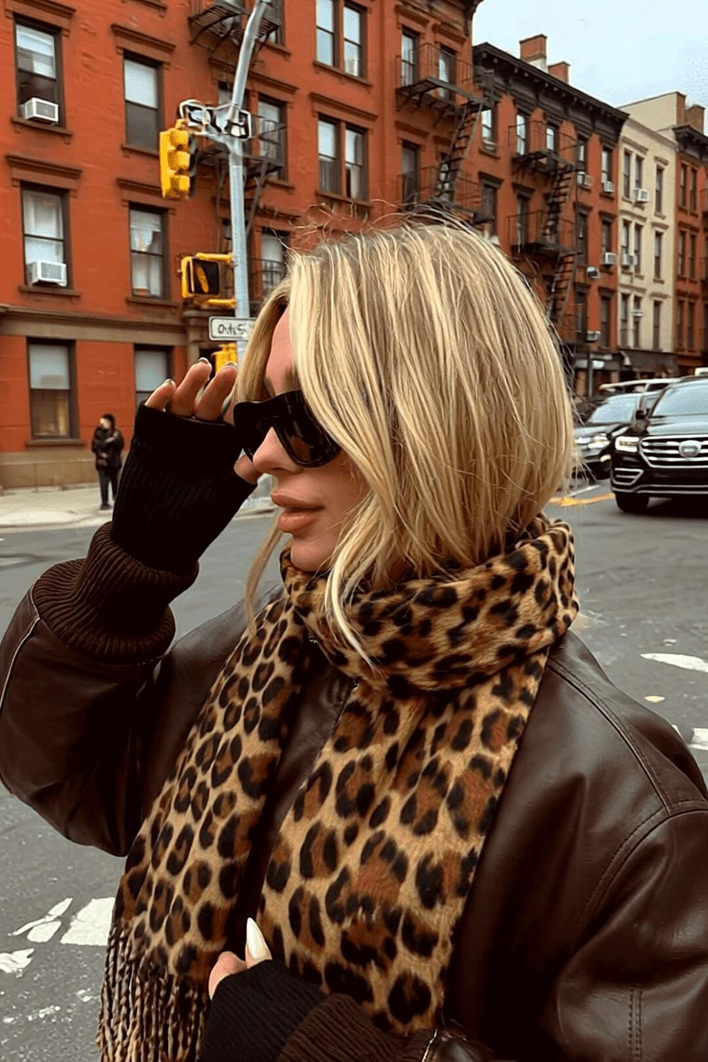 Marais leopard scarf and brown leather bomber on a New York-style street corner with brownstones and fire escapes — Amavé.