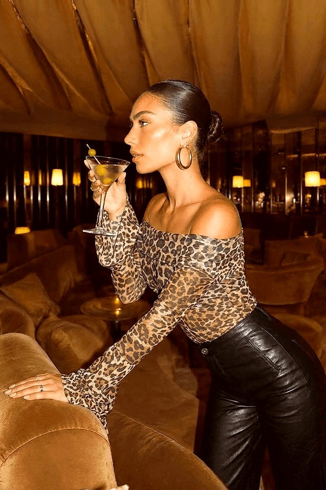 Marseille leopard silk Bardot top in profile, seated with a martini, warm candlelit lounge — Amavé.